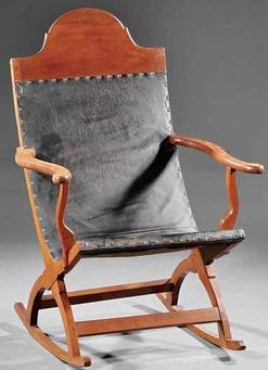 Furniture: A Louisiana carved cherrywood campeche rocking chair, early 19th century, distinctive architectural half-round crest, continuous back and seat with leather [sling] upholstery and nailhead trim, serpentine arms and supports over curule rocker base, pegged and tenoned construction. 